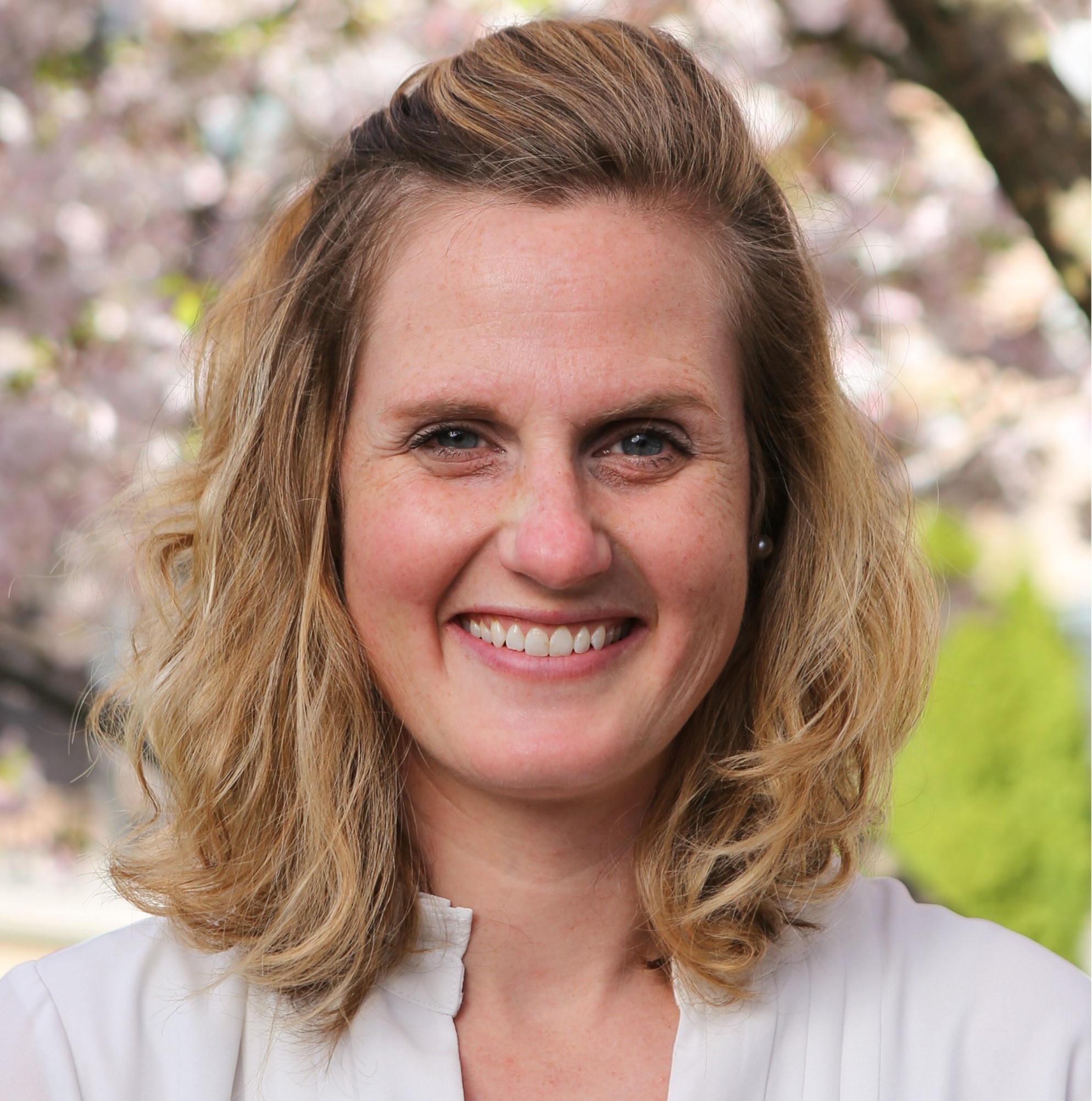 Smiling woman outdoors with trees in the background.